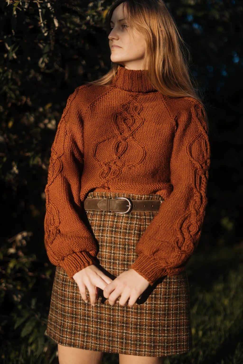 Big Kelpie Sweater, a rust cabled roll-neck worn with a check skirt in evening light